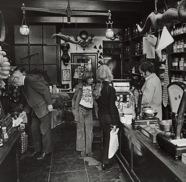 interieur jaren 70 zwart-wit foto aanzicht van buiten naar binnen. Klanten en personeel in de winkel van der pigge