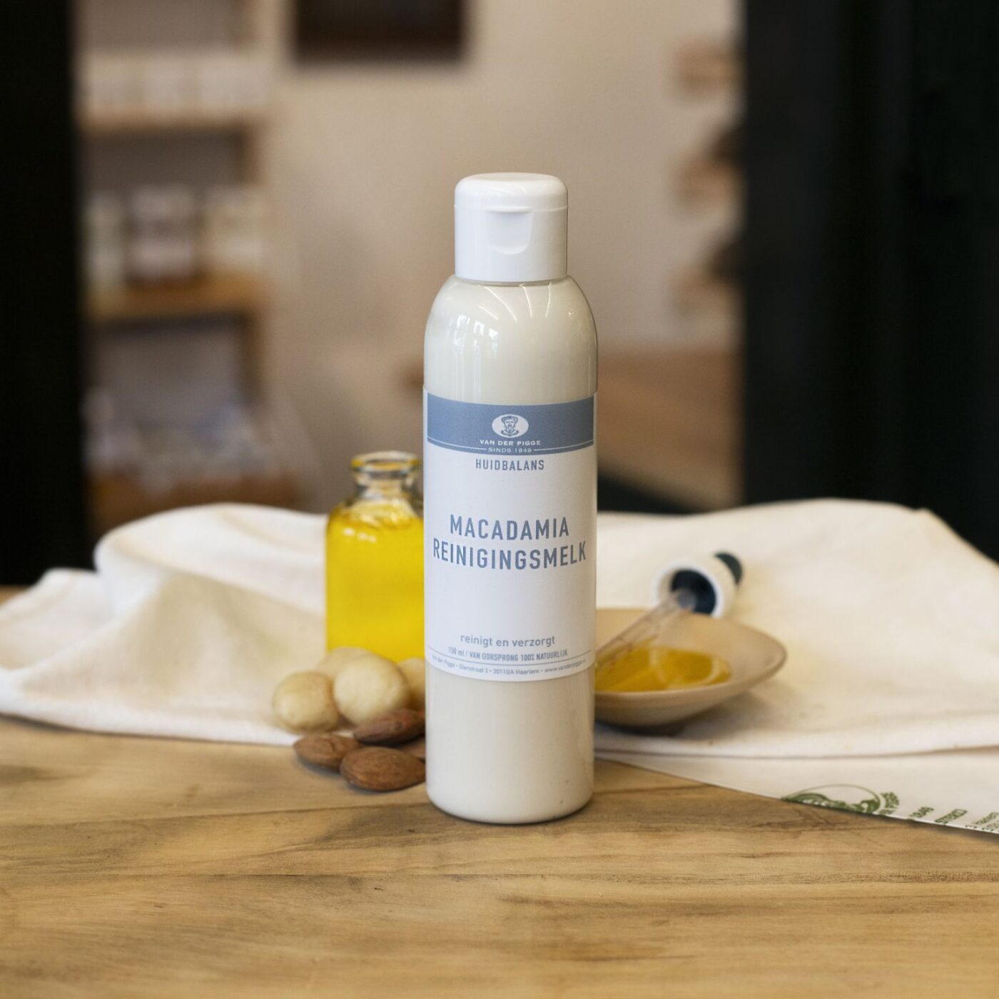 Transparante plastic fles Macadamia reinigingsmelk Huidbalans op houten ondergrond met decoratie witte doek, schaaltje kruiden en flesje gele olie