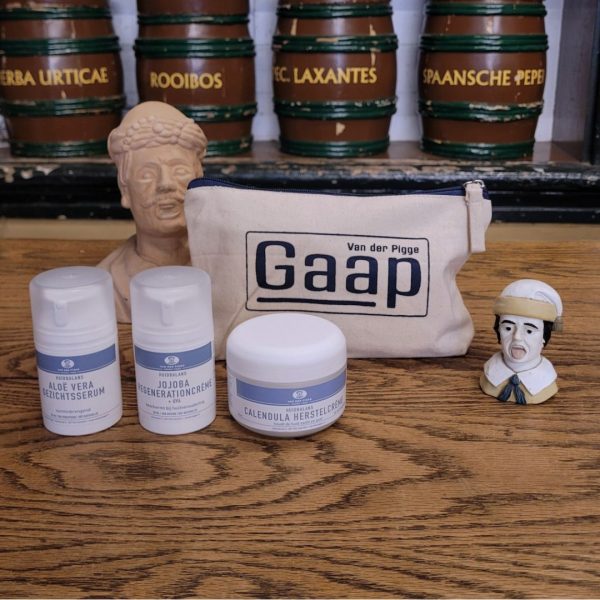 Voordeelset met 3 huidproducten zoals aloe vera serum, calendula herstelcreme en jojoba regenerationcreme in katoenen etui met gaap erop op houten toonbank met decoratieve gapertjes