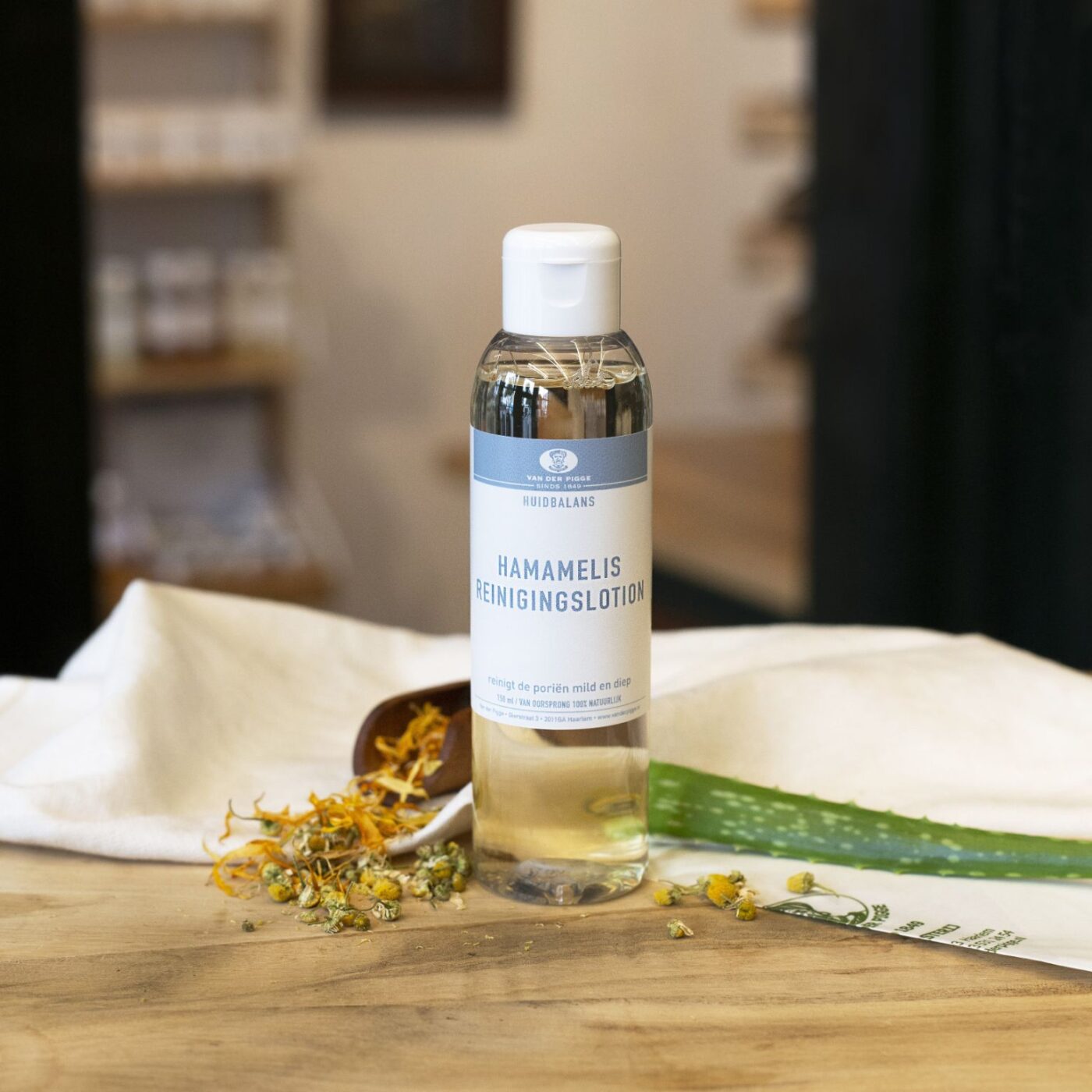 Transparante plastic fles Hamamelis reinigingslotion voor gezicht Huidbalans. Op houten ondergrond met aloe vera en kruiden ter decoratie