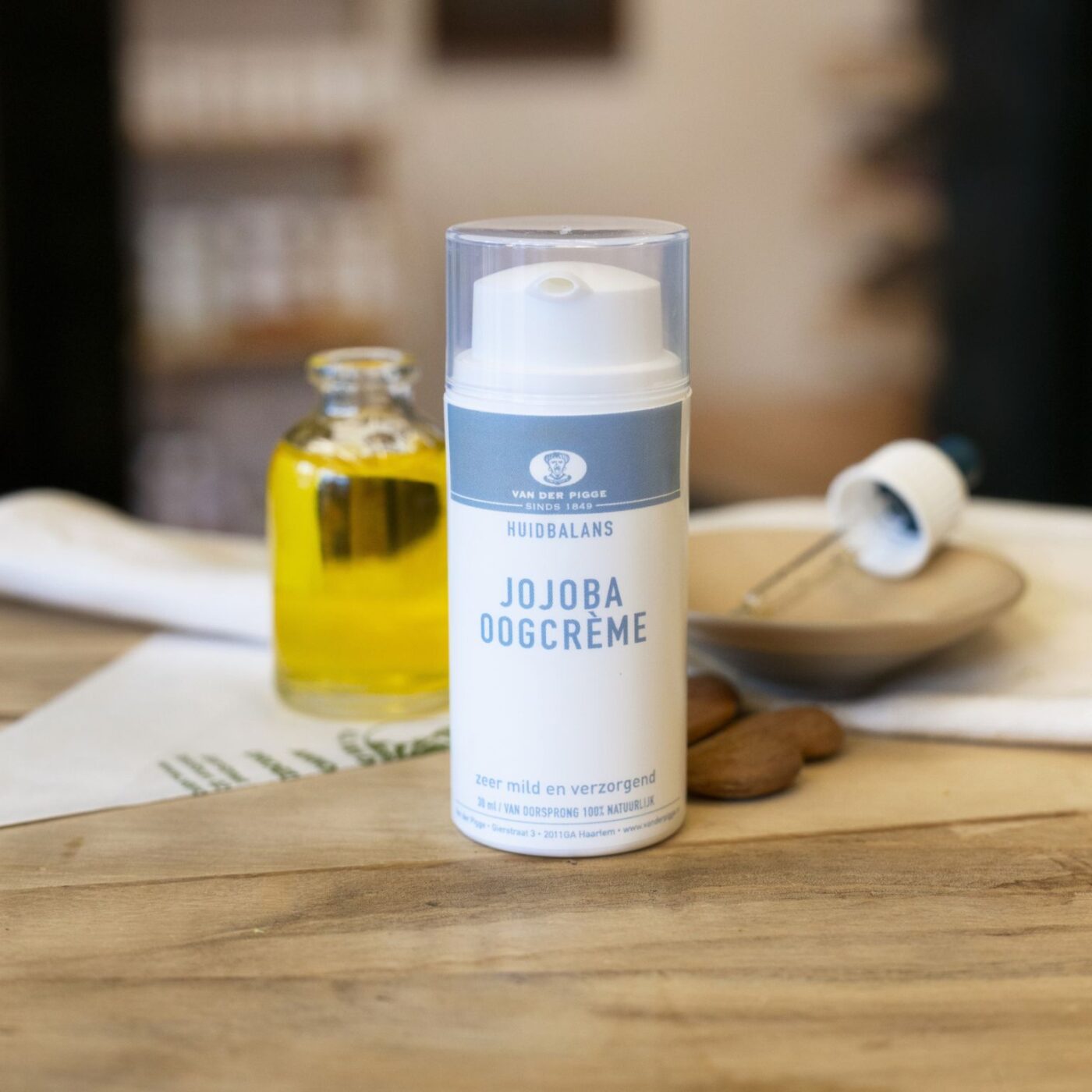 Witte plastic pompflacon jojoba oogcrème huidbalans 30 ml op houten toonbank met flesje olie en pipet