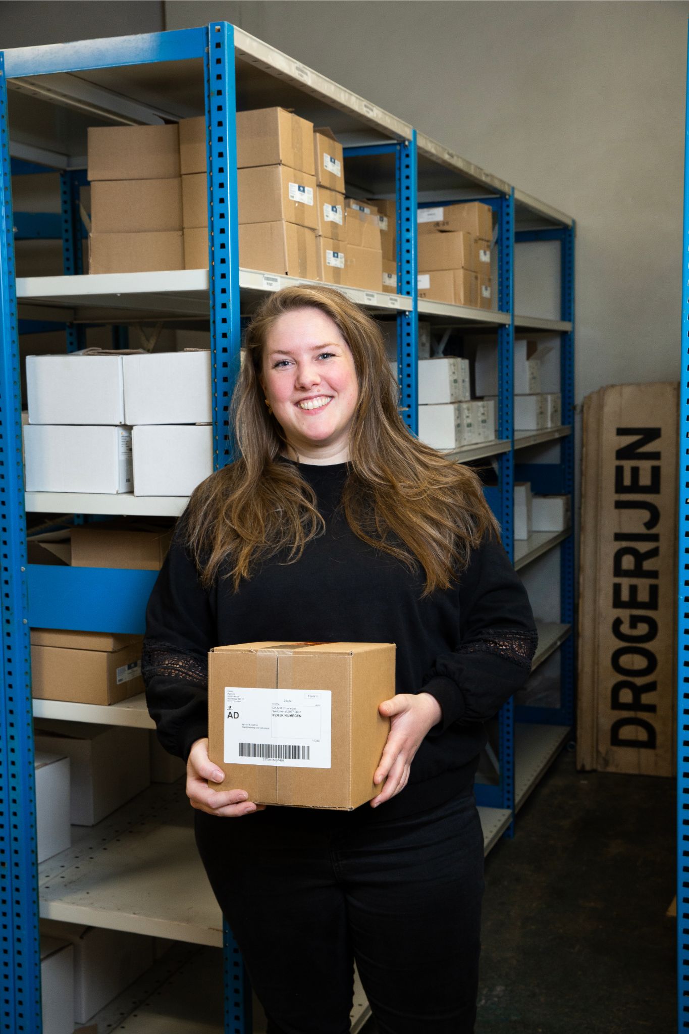 Lachend personeelslid Vera in het magazijn met een doos in de handen