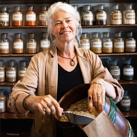 lachende Kitty medewerker winkel met stofjas en opgestoken grijs haar voor de kast met stopflessen