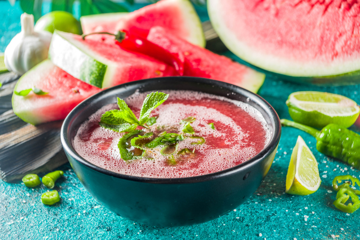 Zomer koude watermeloen smoothie gazpacho soep, marineblauwe achtergrond met plakjes watermeloen, limoen en kruiden
