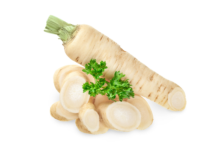 een hele en gesneden wortelpeterselie met groen op een witte achtergond