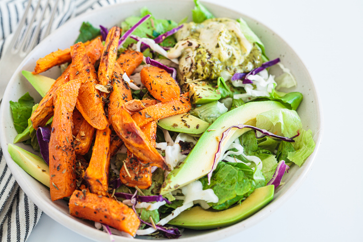 Gebakken zoete aardappelpartjes met avocado- en hummusdip. Gezonde veganistische lunchsalade.