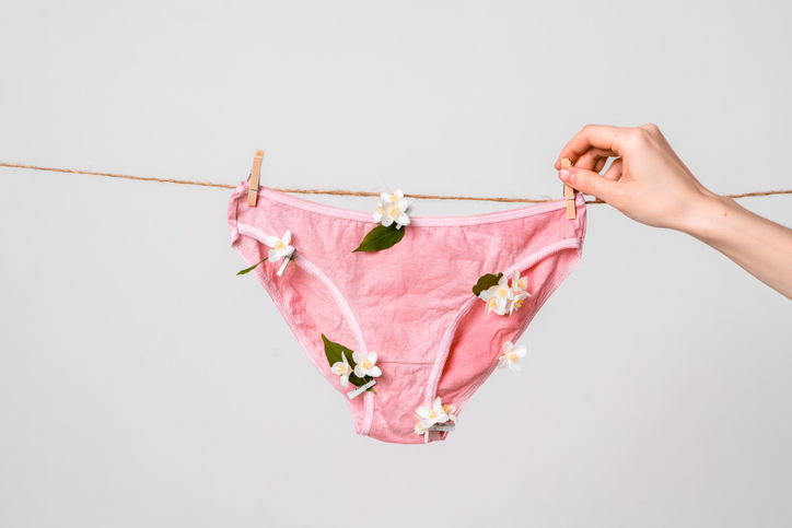 vrouw hangt onderbroek aan waslijn met bloemen, lichen sclerosus en lichen planus thema