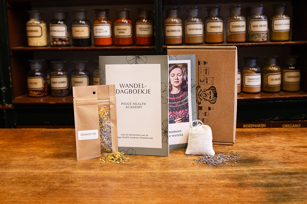 Sfeerbeeld van het wandel meditatie pakket meditatiewandeling met zakje thee, lavendelzakje, wandeldagboekje en flyer in de winkel met houten ondergrond