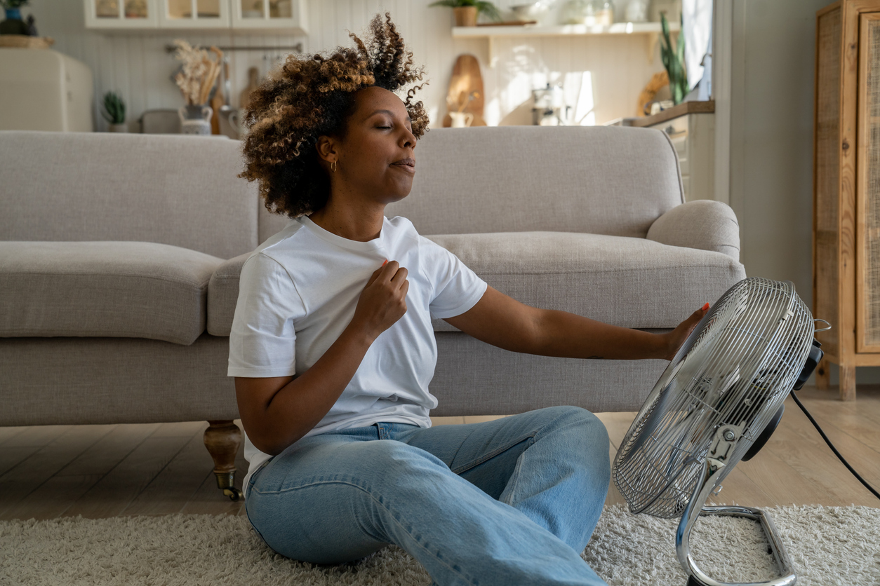 Vrouw wapperend met haar tshirt zichzelf koelte toeblazend met een ventilator