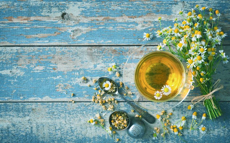 Glazen kopje kamille thee op een mooie blauwe oud houten tafel, omring met kamillie bloemtjes